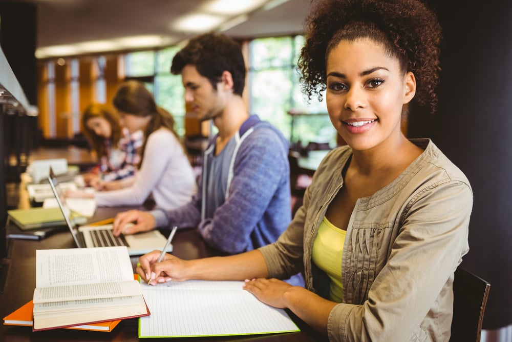 Student looking at camera while studying with classmates in library